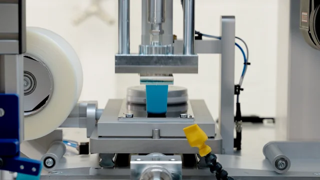 Close-up of a pad printing machine in operation, showing the blue pad descending towards the cliche plate, illustrating the precise ink transfer mechanism for industrial printing by Automark.