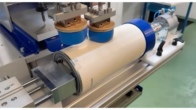 Close-up of a round part securely held in a custom-designed fixture within a pad printing machine, demonstrating precision setup for accurate printing, distributed by Automark.